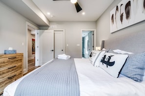 Een slaapkamer met een bed, een dressoir, een plafondventilator en een deur naar een andere kamer.