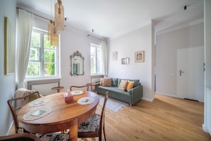A room with a wooden dining table, chairs, a sofa, and a large window with curtains. - Mostowa Old Town Apartment, Warsaw (Warszawa)