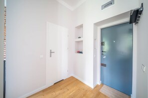 En hall med en vit dörr, en blå dörr och en hylla med dekorativa föremål.