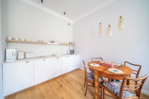 A dining area with a wooden table and chairs, a white cabinet with kitchen appliances, and a wall-mounted light fixture. - Mostowa Old Town Apartment, Warsaw (Warszawa)
