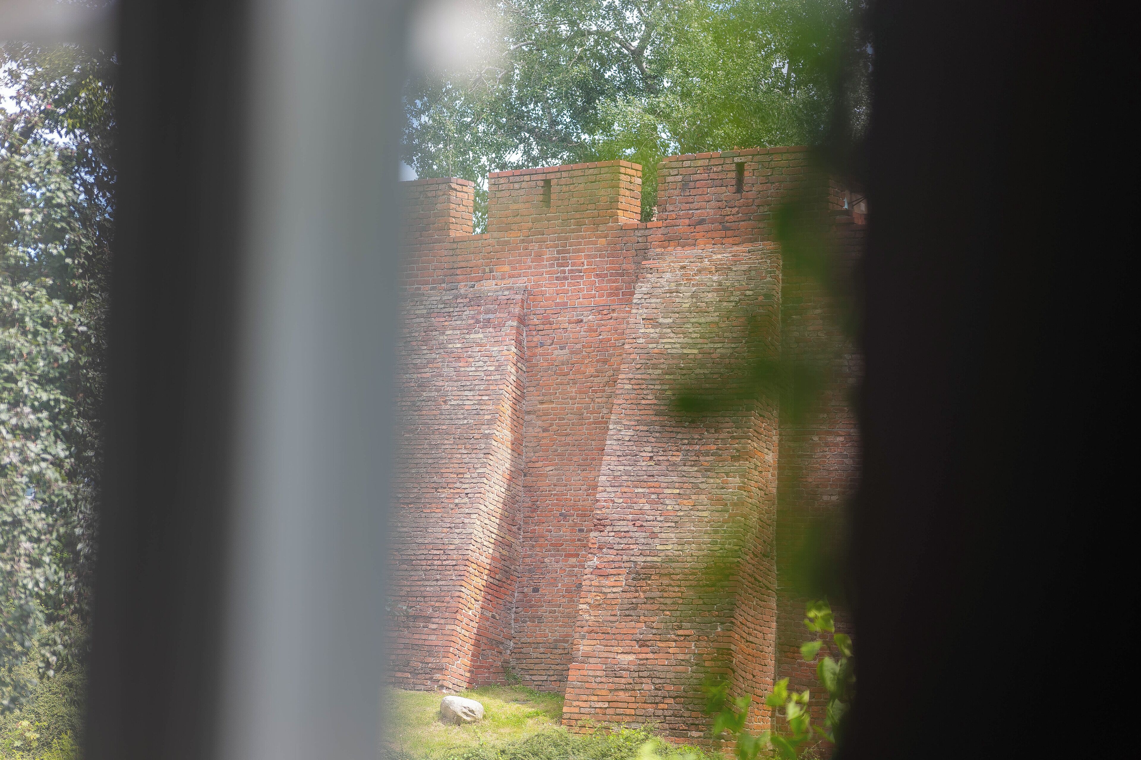 A brick wall with a small opening, surrounded by greenery.