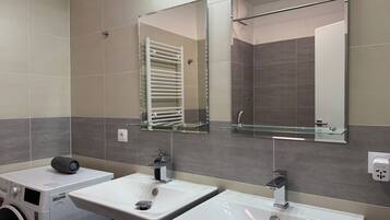 A modern bathroom with two sinks, a glass shelf, a towel rack, and a washing machine.