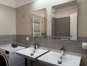 Uma casa de banho moderna com duas pias, uma prateleira de vidro, um porta-toalhas e uma máquina de lavar roupa.