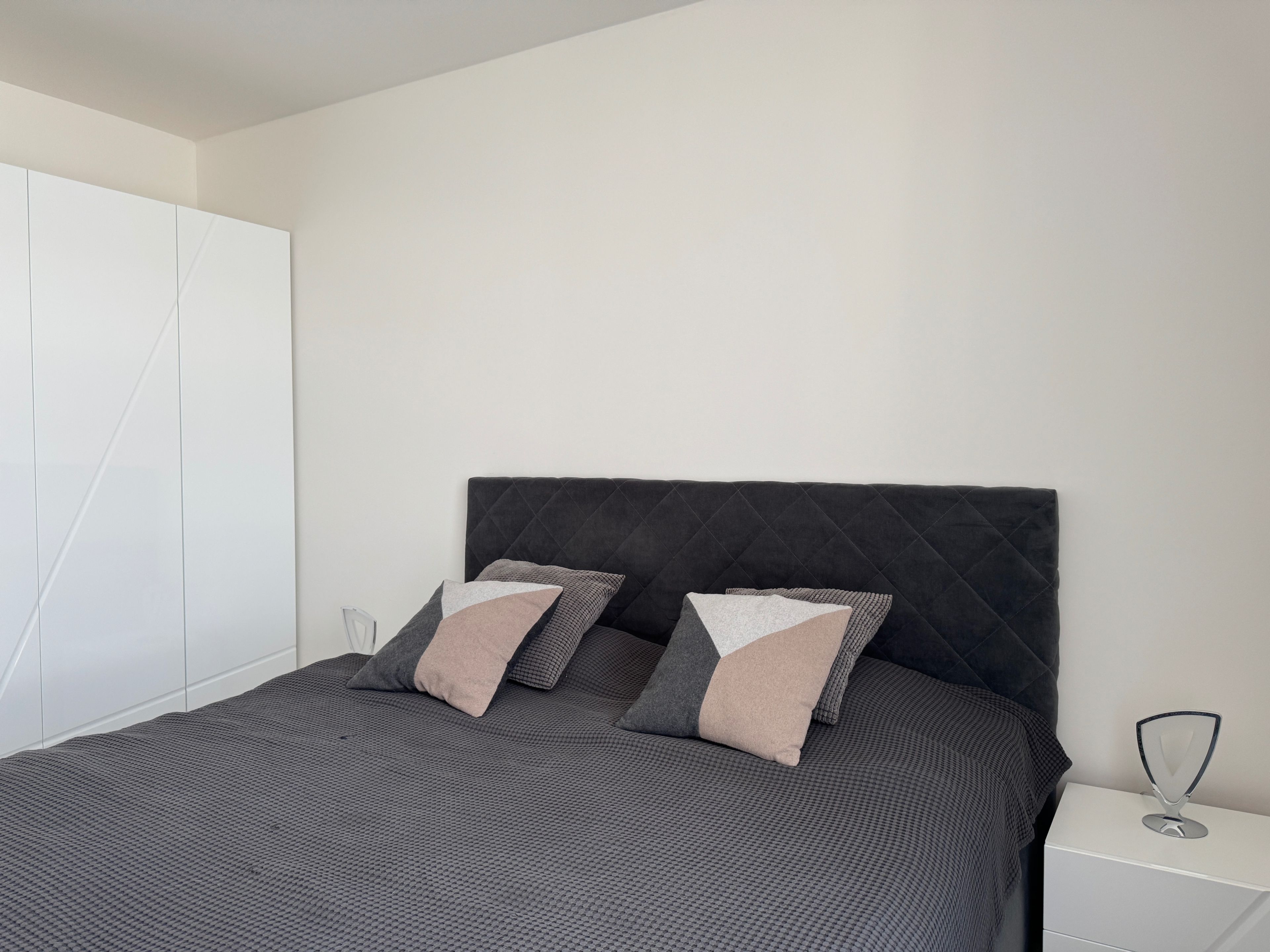 Een moderne slaapkamer met een bed, kussens, een nachtkastje en een kledingkast.