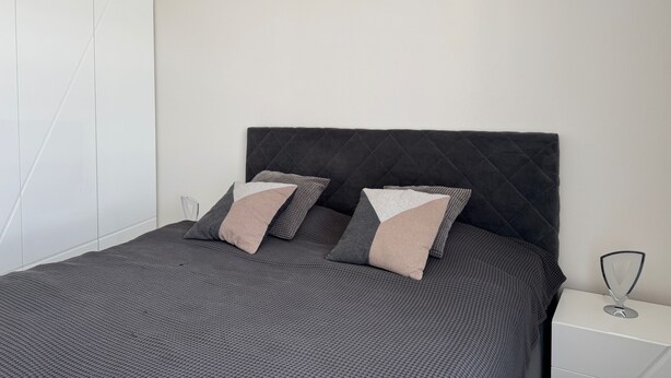 Un dormitorio moderno con cama, almohadas, una mesita de noche y un armario.