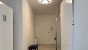 Un pasillo con un radiador, una puerta y un taburete pequeño.