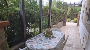 A covered patio with a table and chairs, surrounded by a stone wall and a metal fence.