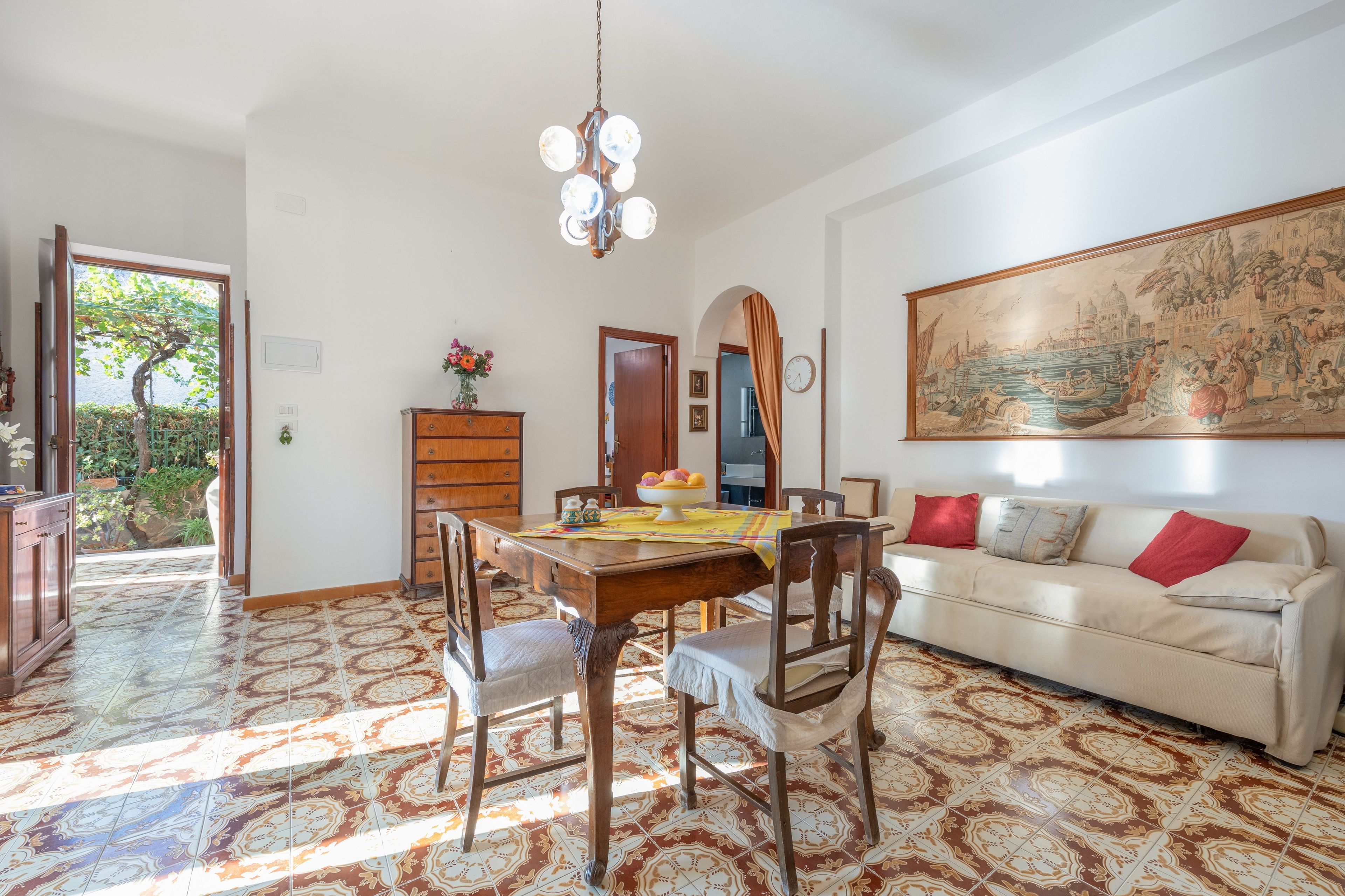 Un comedor con mesa y sillas de madera, una araña y un cuadro grande en la pared.