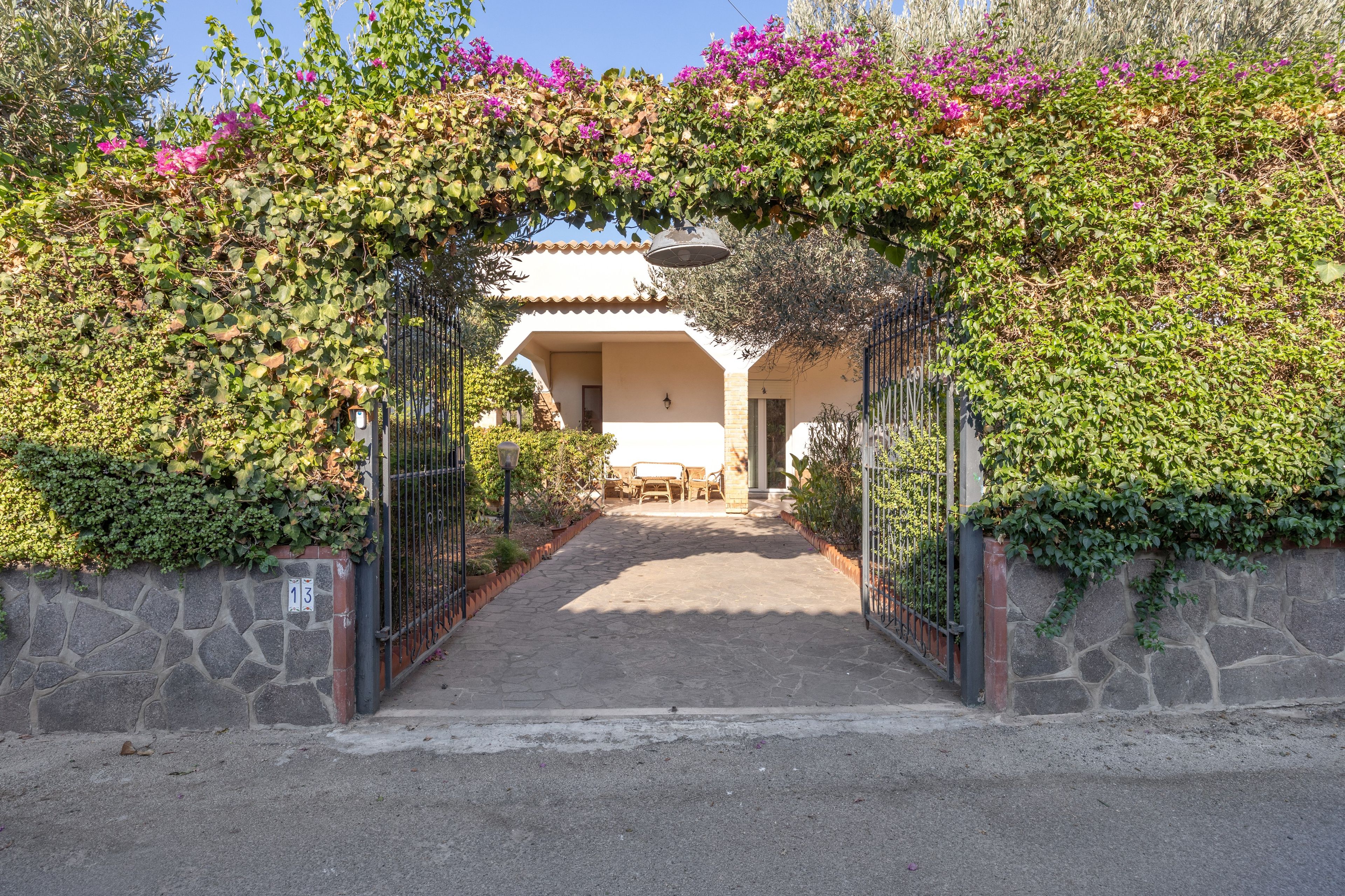 Un chemin menant à un bâtiment à l’architecture traditionnelle, entouré d’une végétation luxuriante et de plantes en fleurs.