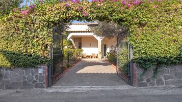 Un chemin menant à un bâtiment à l’architecture traditionnelle, entouré d’une végétation luxuriante et de plantes en fleurs.
