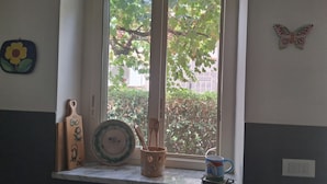 A kitchen window with a view of greenery, a flower decoration, and a butterfly ornament. - Villa 'Villetta Ninetta' with Mountain View, Wi-Fi and Air Conditioning (Carini(Pa))