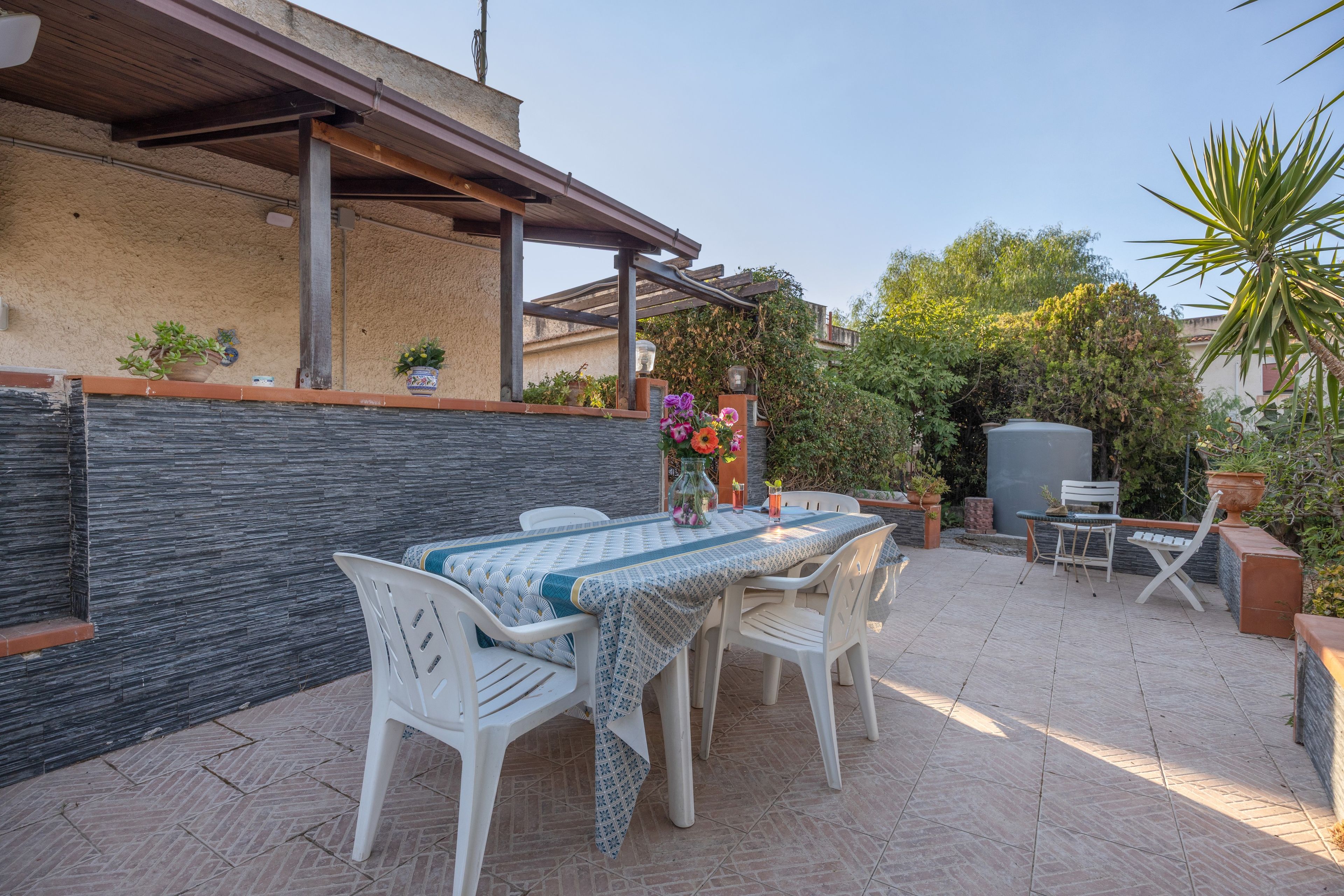Eine Außenpatio mit Tisch und Stühlen, umgeben von Blumentöpfen und einer Steinmauer.