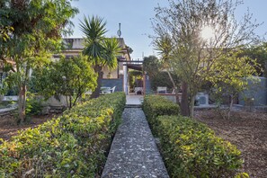 A pathway leading to a building with a covered entrance, surrounded by well-maintained hedges and trees.