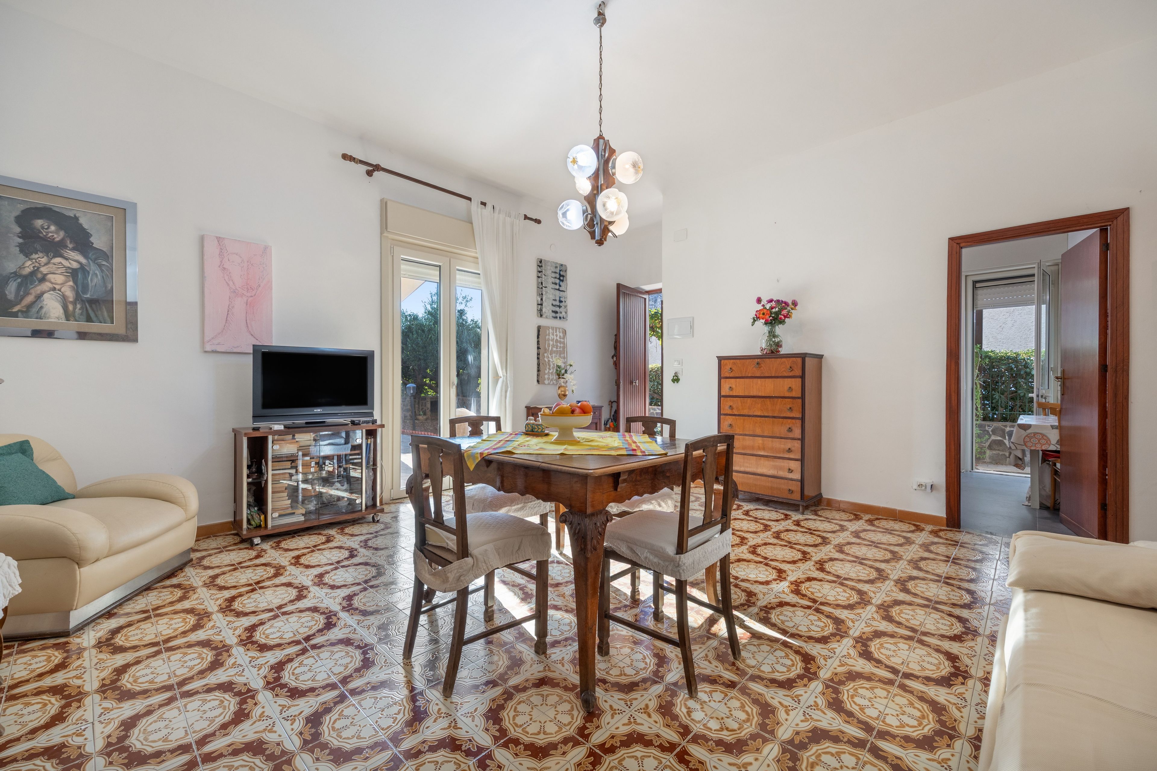 Una sala de estar con una mesa de comedor, sillas, un sofá, un televisor y obras de arte en las paredes.