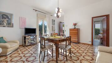 Una sala de estar con una mesa de comedor, sillas, un sofá, un televisor y obras de arte en las paredes.