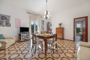 A living room with a dining table, chairs, a sofa, a TV, and artwork on the walls.