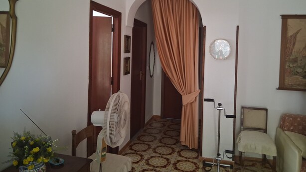 A room with a patterned floor, a standing fan, a chair, a table with a vase of flowers, and a door leading to another room. - Villa 'Villetta Ninetta' with Mountain View, Wi-Fi and Air Conditioning (Carini(Pa))