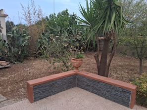 Een hoek van de tuin met een stenen plantenbak, verschillende planten en een boom.