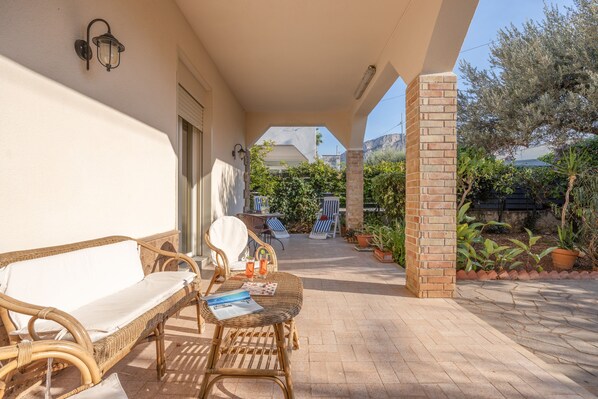 A covered outdoor seating area with wicker furniture, a table, and a chair.