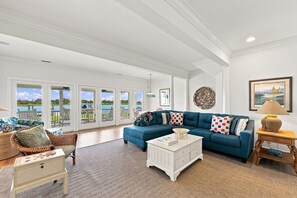 A spacious living room with a blue sofa, wicker furniture, and a view of a lake through large glass doors. - 1524 Front Street-Sound Front with Dock (Beaufort)