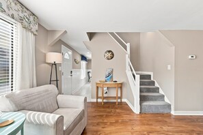 A living room with a sofa, a lamp, a table with a decorative item, and a staircase. - Laid Back Laurel-Pet Friendly in Beaufort, NC (Beaufort)