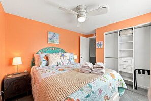 A bedroom with a bed, a ceiling fan, a nightstand, a lamp, a wall with a painting, and a wardrobe. - Laid Back Laurel-Pet Friendly in Beaufort, NC (Beaufort)