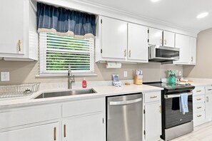 A modern kitchen with white cabinets, stainless steel appliances, and a window with blinds. - Laid Back Laurel-Pet Friendly in Beaufort, NC (Beaufort)