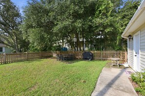 Ein Garten mit Holzzaun, Grill und Terrassentisch.