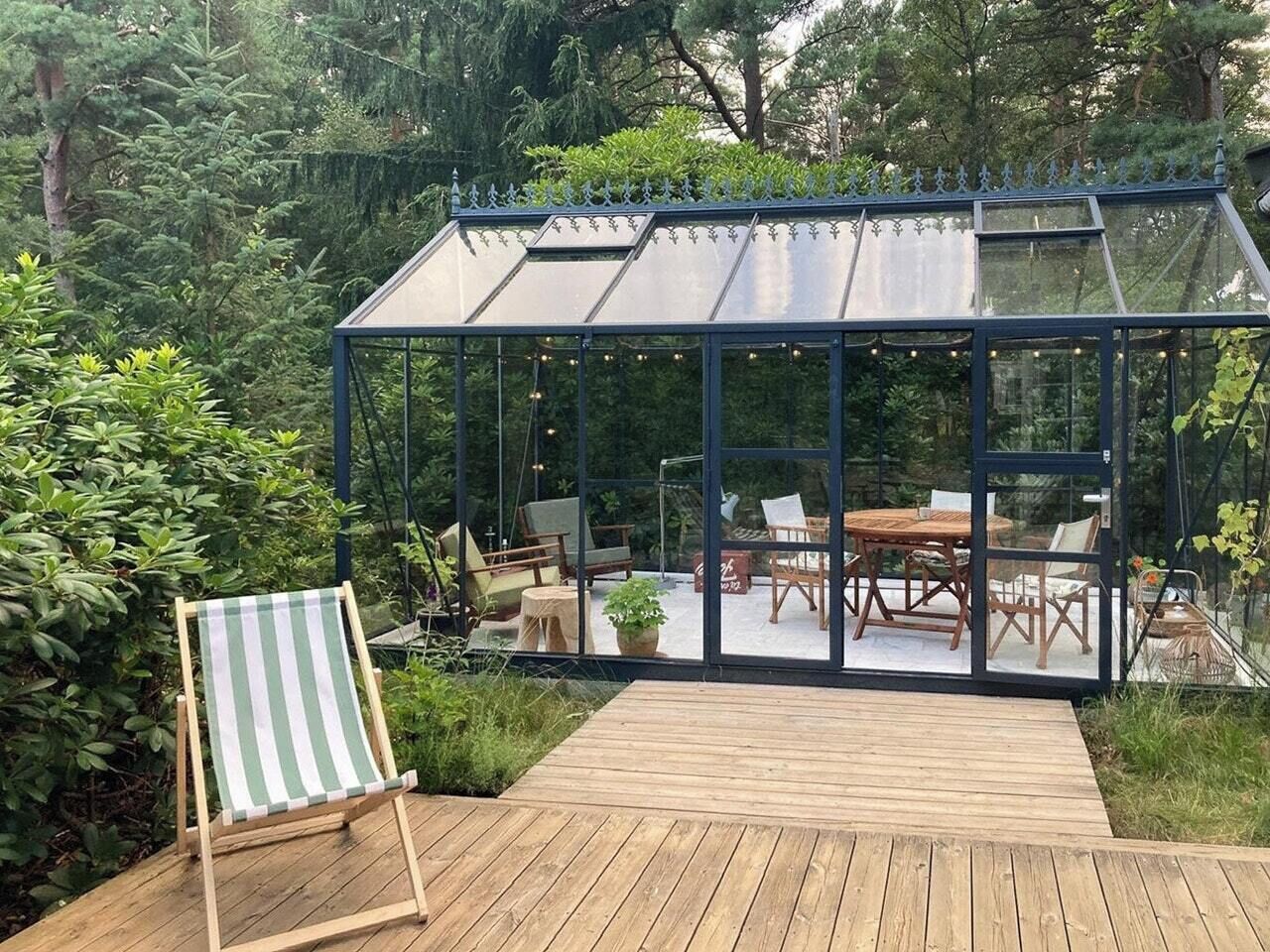 A conservatory with a wooden deck, seating area, and glass walls.