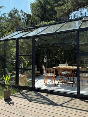 Ein Wintergarten mit Glasdach, Holzterrasse und einem Tisch mit Stühlen.
