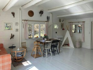 Een knus ingerichte kamer met een houten tafel, stoelen, een raam met gordijnen, een tent en diverse wanddecoraties.