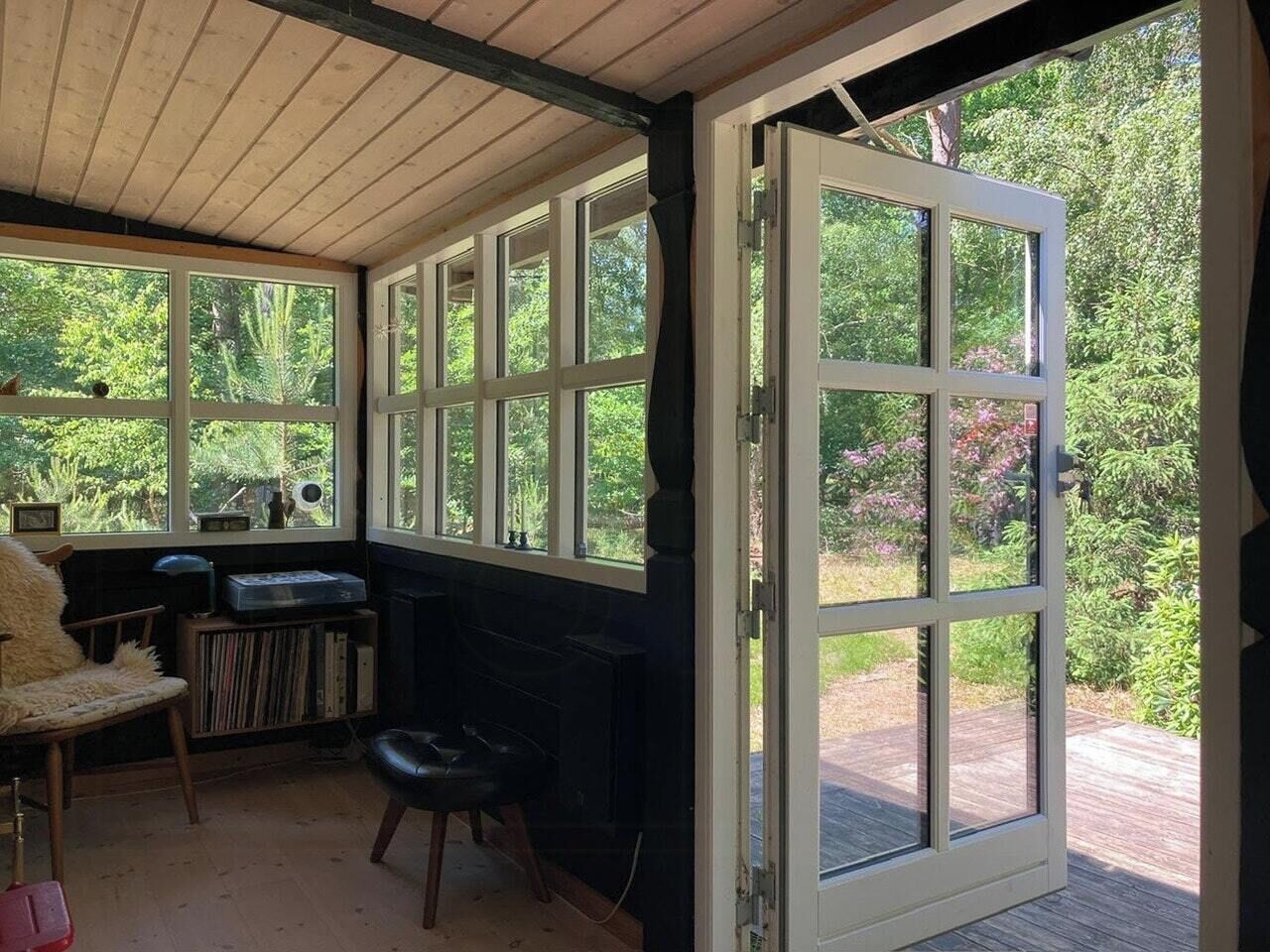 A room with a wooden ceiling, a fireplace, a bookshelf, a chair, and a large open door leading to an outdoor area.