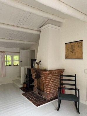 Ein Zimmer mit Kamin, einem Sessel und einem fenster mit Vorhängen.