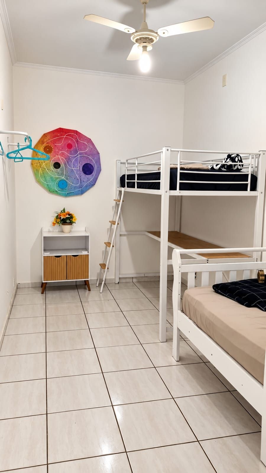 Habitación con literas, ventilador de techo, decoración de pared colorida, un mueble de madera pequeño y piso de baldosas.
