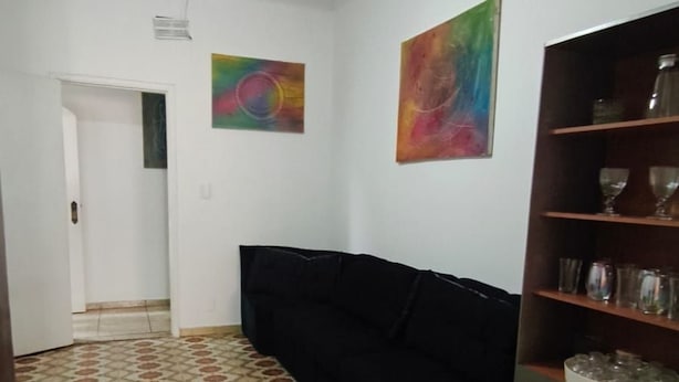 A room with a black sofa, a ceiling fan, a tiled floor, and a bookshelf. - Nomah Hostel 2 (São José do Rio Preto)