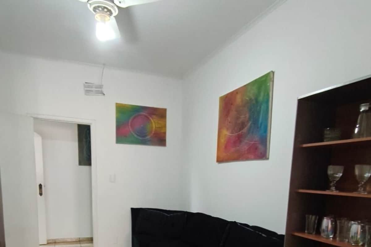 Una habitación con ventilador de techo, un sofá negro, una estantería y un suelo estampado.