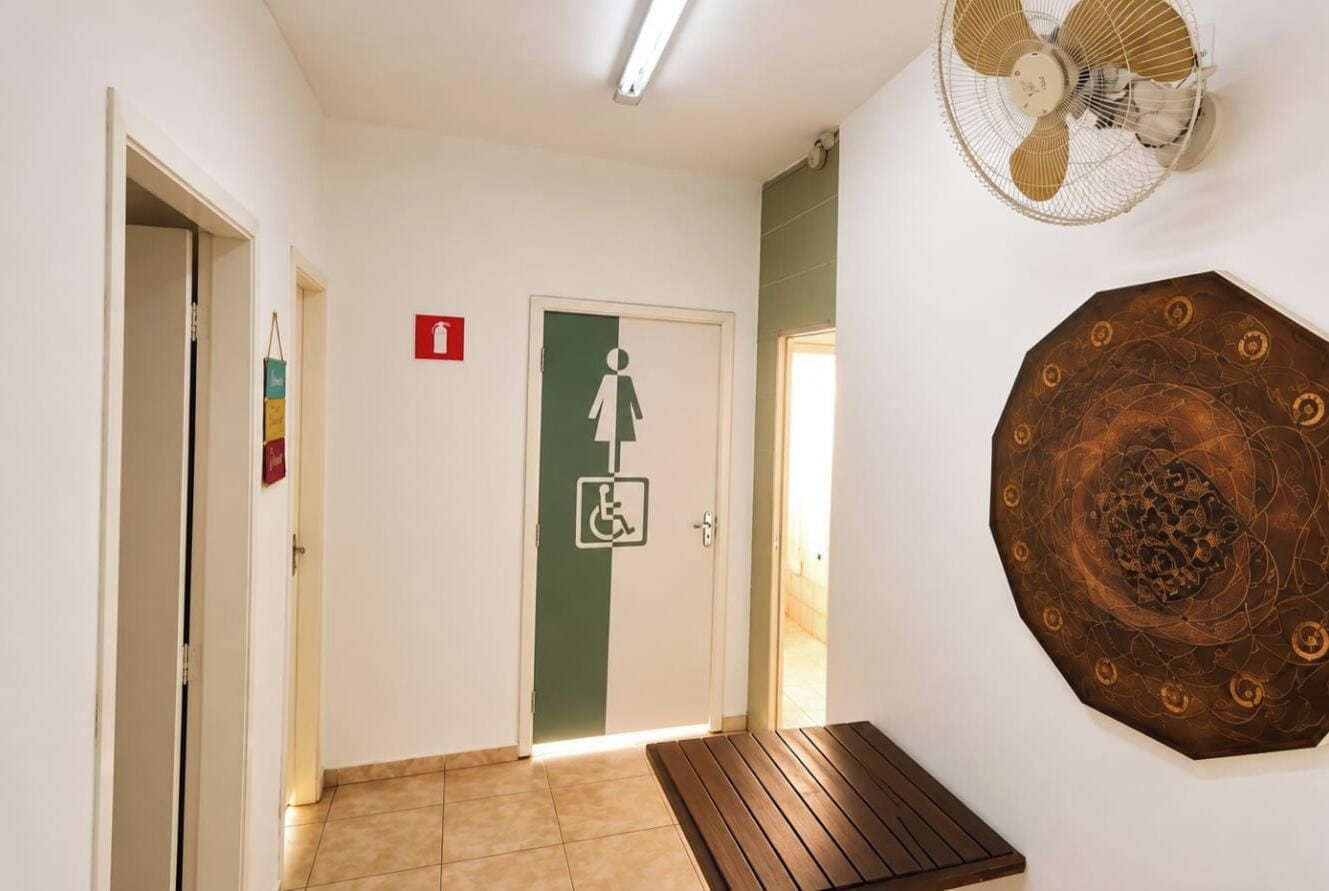 Corredor com porta acessível para cadeiras de rodas, alarme de incêndio e um detalhe decorativo na parede.