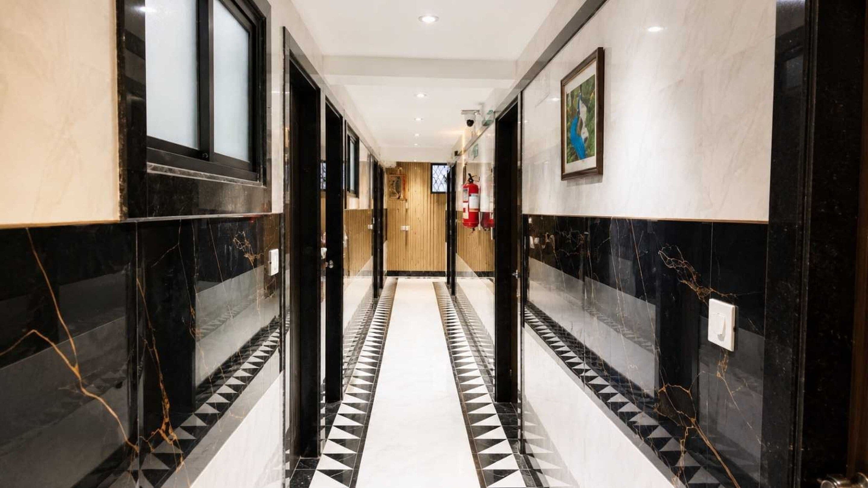 A corridor with black and white patterned flooring, doors on both sides, and a fire extinguisher mounted on the wall.