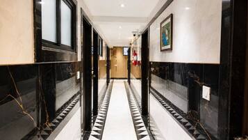 A corridor with black and white patterned flooring, doors on both sides, and a fire extinguisher mounted on the wall.