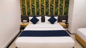 A hotel room with a bed, a bedside table with a phone, a trash bin, and a wall with vertical greenery. - Classic Hanspura Bus Terminal (Ahmedabad)
