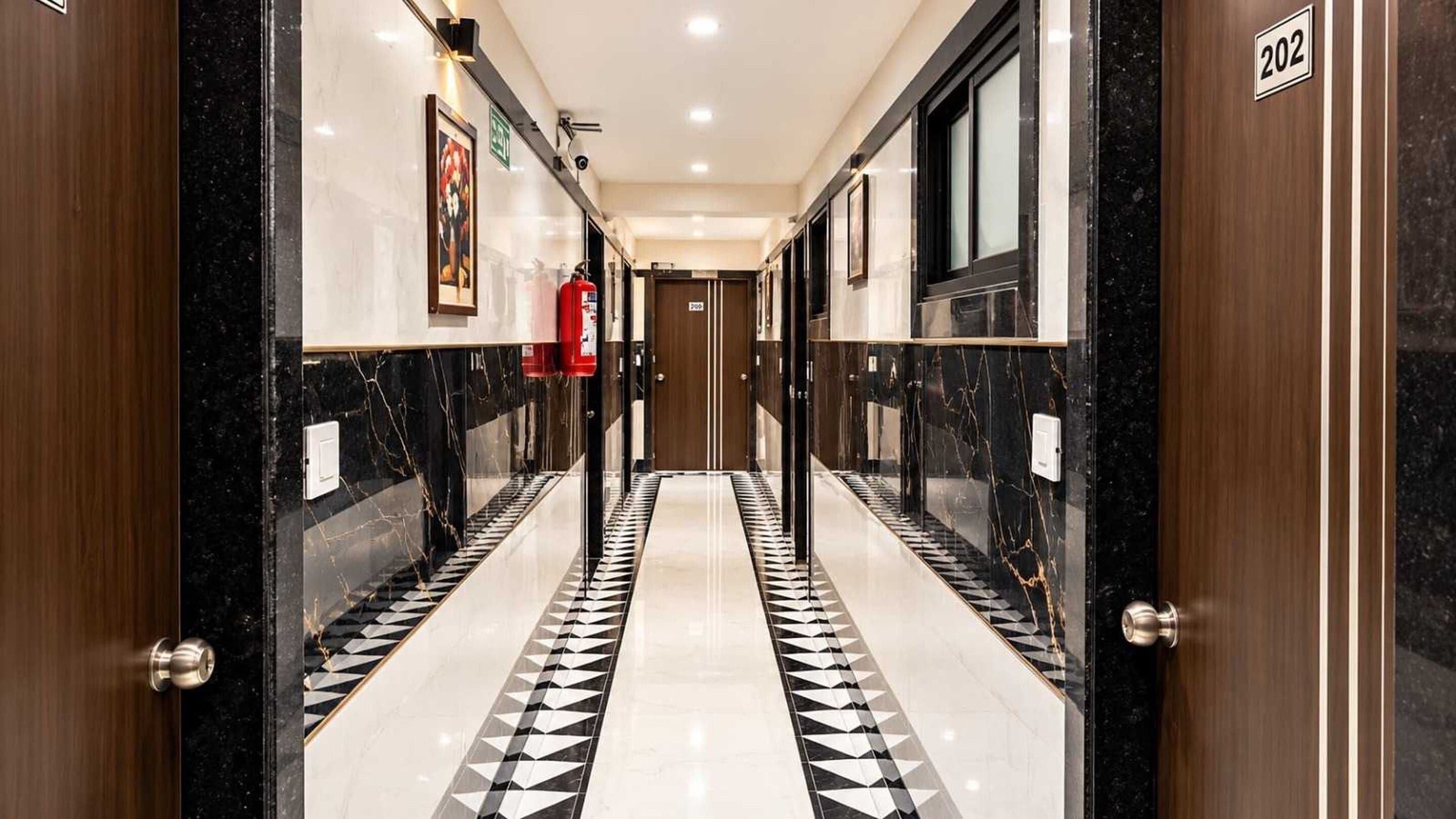 A corridor with a black and white patterned floor, wooden doors, and a fire extinguisher on the wall.