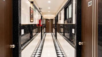 A corridor with a black and white patterned floor, wooden doors, and a fire extinguisher on the wall.
