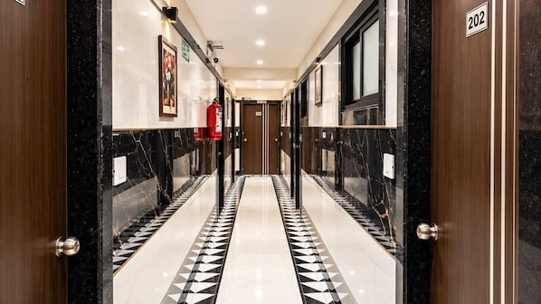 A corridor with a black and white patterned floor, wooden doors, and a fire extinguisher on the wall. - Classic Hanspura Bus Terminal (Ahmedabad)