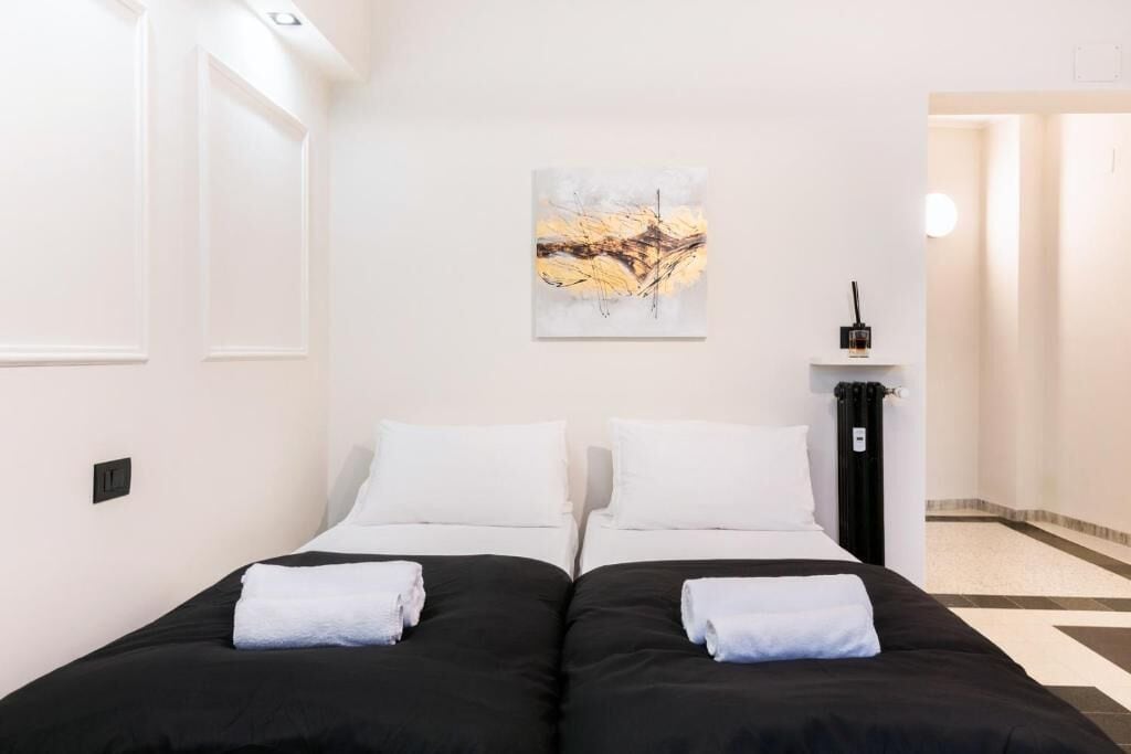 Ett hotellrum med två sängar, vita sängkläder, en tavla på väggen och ett element.