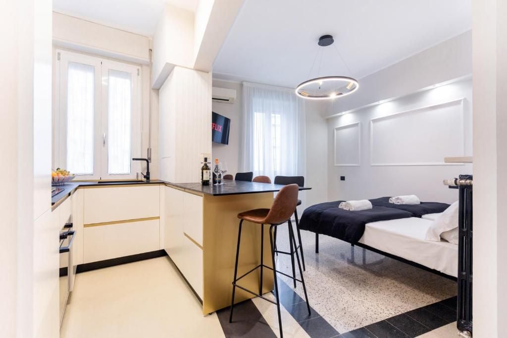 A compact hotel room with a kitchenette, a bed, a small bar area, and a TV mounted on the wall.