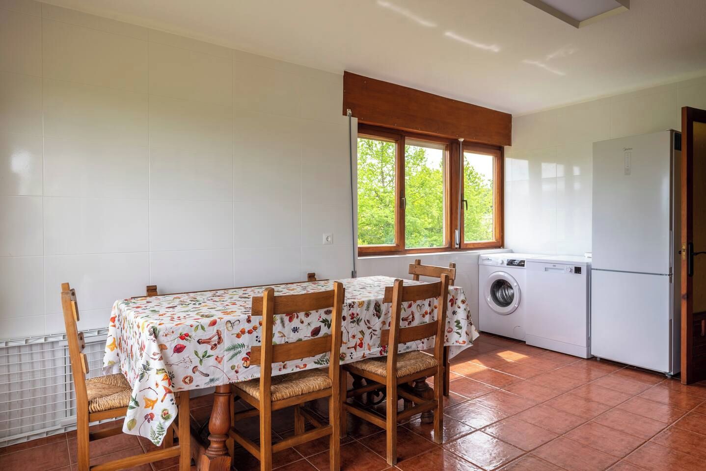 Une cuisine équipée d’une table et de chaises, d’un lave-linge et d’une fenêtre donnant sur un espace verdoyant.
