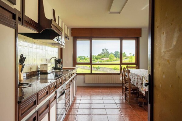 A kitchen with a large window, a dining table, and a view of a green landscape.