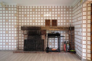 A room with a tiled wall, a fireplace, and a small table with a broom and a bag of charcoal.