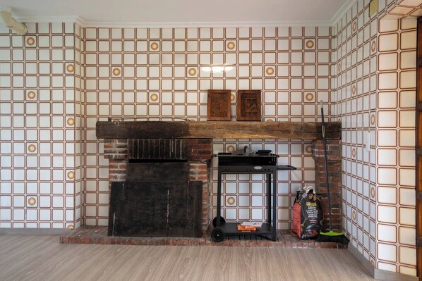 A room with a tiled wall, a fireplace, and a small table with a broom and a bag of charcoal.