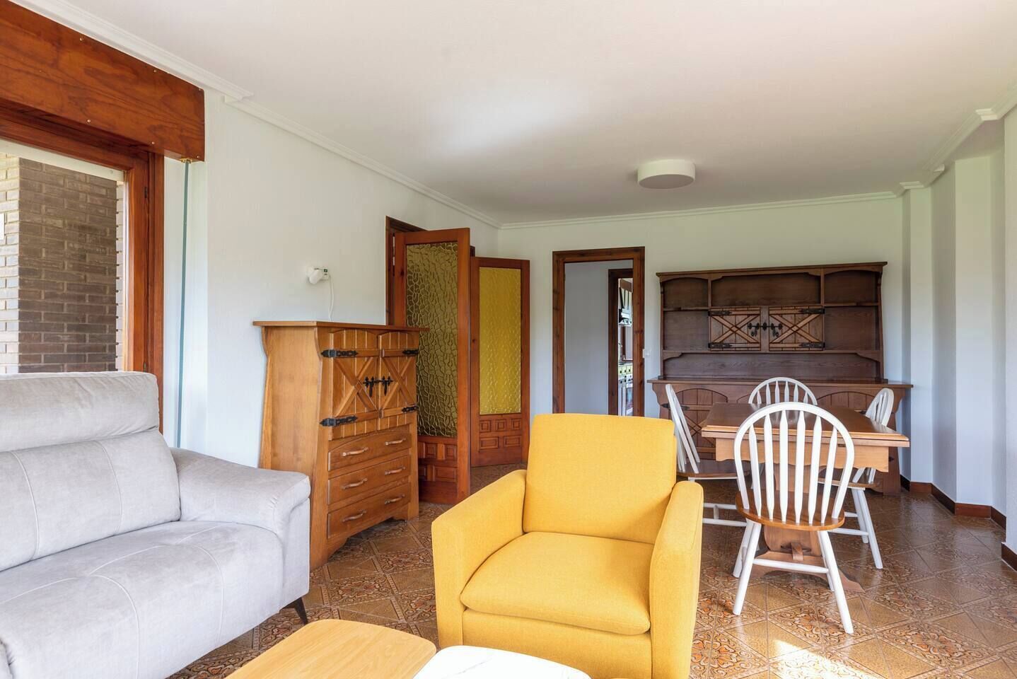 A living room with a sofa, a yellow armchair, and a dining area with a table and chairs.